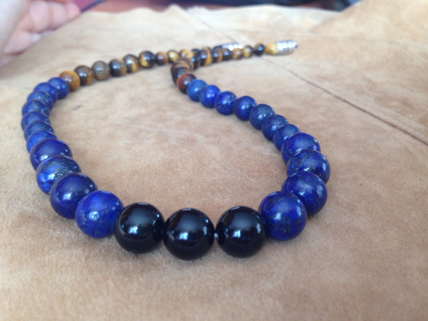 Stone necklace with lapis lazuli, black onyx, and tiger's eye beads on a suede background