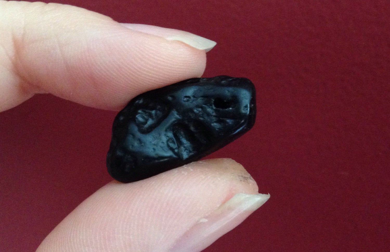 Small irregular black TEKTITE tumblestone held between fingers promoting lucid dreaming and wisdom