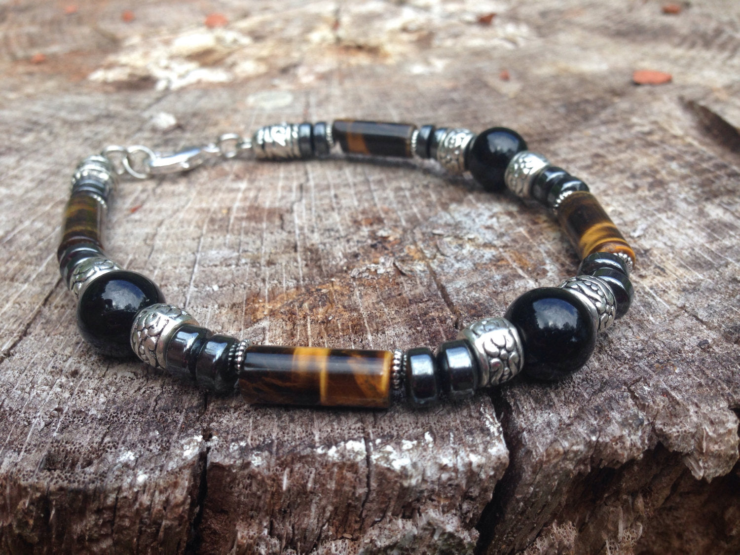 Men's bracelet featuring tigers eye, black onyx, and hematite stones on a rustic wooden surface