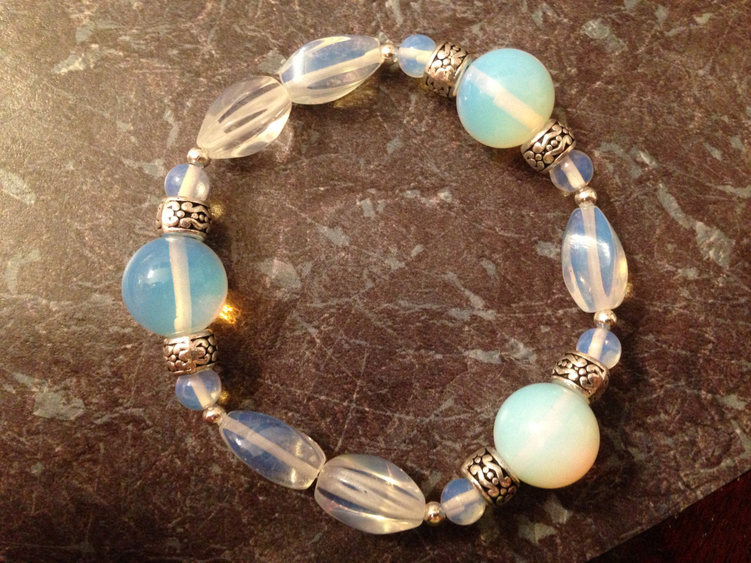 Opalite bracelet with varied bead sizes and silver accents on brown textured surface