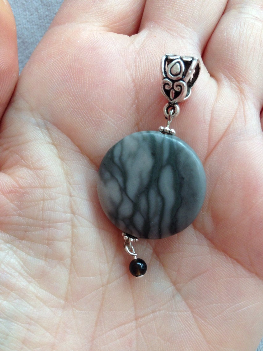 Pendant canyon gray marble round disc with black onyx bead held in hand