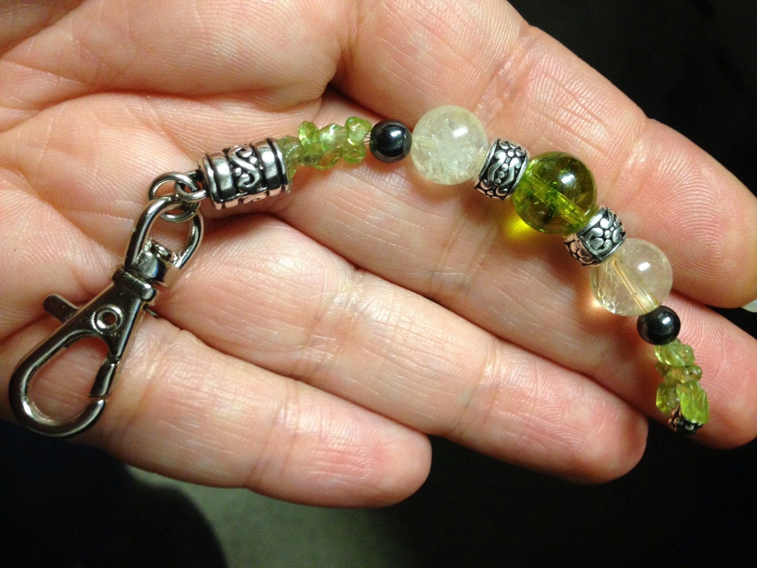 Hand holding a unique purse charm with citrine, peridot, hematite stones and metal clasp