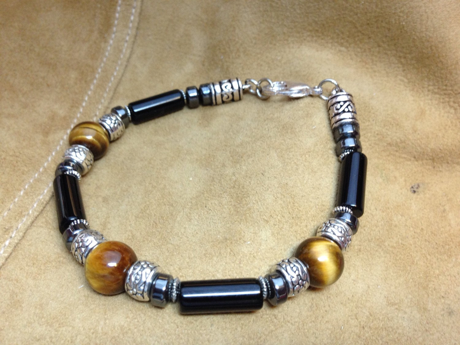Men's bracelet made with tigers eye, black onyx, hematite, and silver accents on beige background