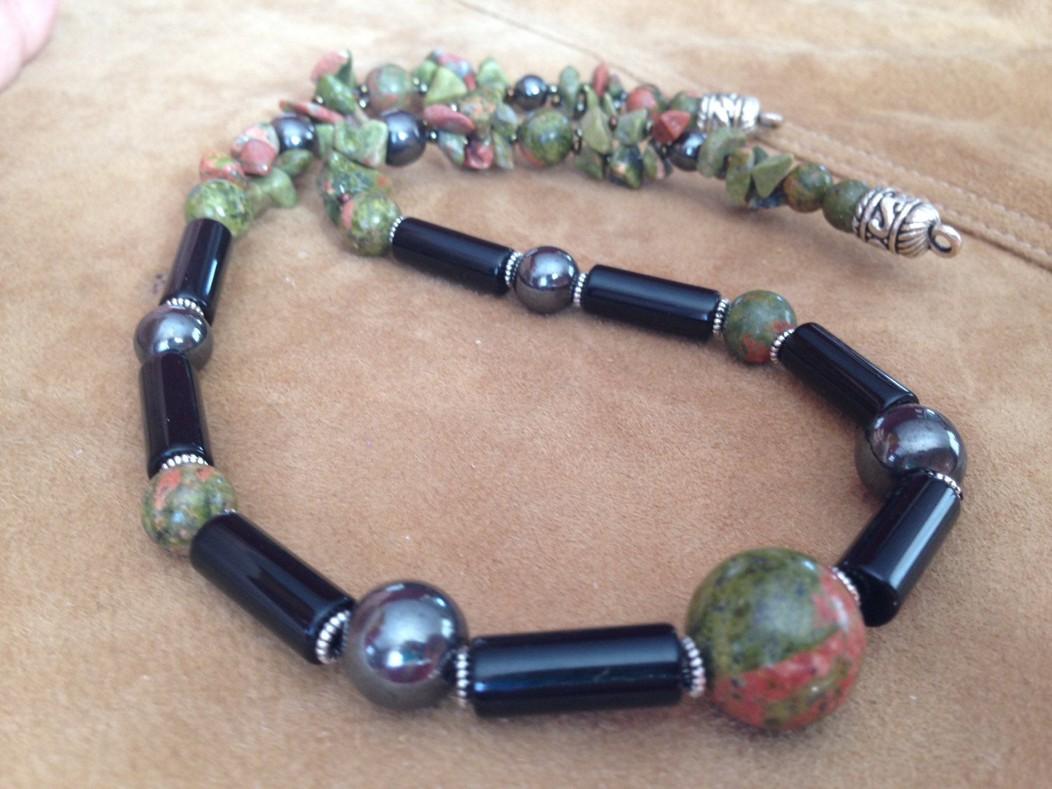 Men's necklace made of Unakite, black onyx, and hematite natural stones on a beige surface
